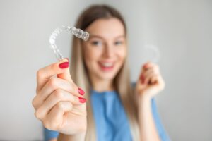 Woman with red nails blurry in background holding Invisalign to foreground